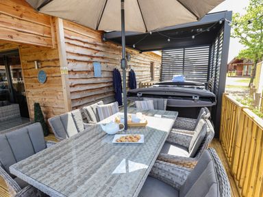 An outdoor patio with a glass table and cushioned chairs under an umbrella at Lake View Lodge in Thorpe-On-The-Hill