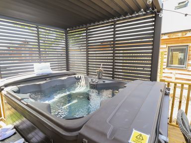 An outdoor hot tub with water inside under a covered structure with slatted walls at Lake View Lodge in Thorpe-On-The-Hill