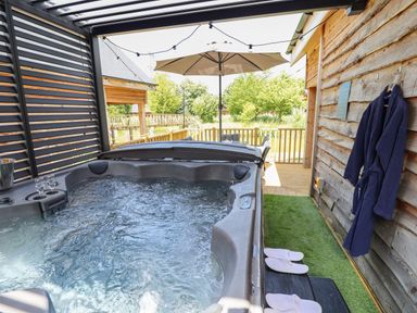 An outdoor hot tub with water bubbling next to a wooden wall with a robe and slippers at Lake View Lodge in Thorpe-On-The-Hill