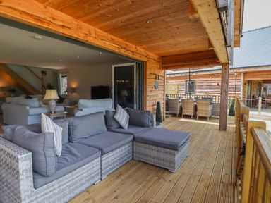 A covered wooden deck with grey cushioned patio sofa and outdoor dining set at Lake View Lodge in Thorpe-On-The-Hill