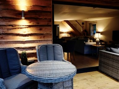 A seating area with wicker chairs and a round table next to a wooden wall and an indoor living room with sofas and lamps at Lake View Lodge in Thorpe-On-The-Hill