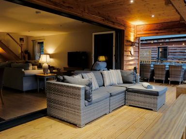A seating area with cushioned wicker sofas on a wooden deck next to an indoor living room at Lake View Lodge in Thorpe-On-The-Hill