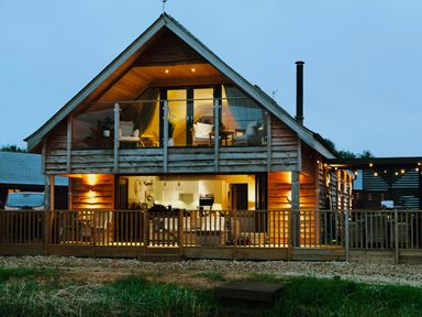 A wooden house with glass balcony and outdoor seating area at Lake View Lodge in Thorpe-On-The-Hill