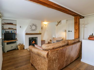 A living room with a leather sofa a fireplace a TV on a cabinet and a staircase at Little Owl Barn in Burford