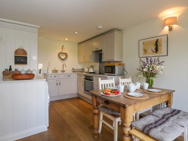 A kitchen with a wooden dining table set with plates and cups and flowers on the table at Little Owl Barn in Burford
