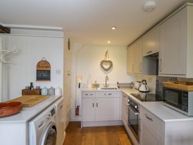 A kitchen with grey cabinets white countertop appliances and wooden floor at Little Owl Barn in Burford