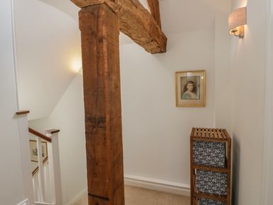 A hallway with a wooden beam a framed painting on the wall a small wooden storage unit and a wall lamp at Little Owl Barn in Burford