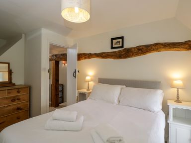A bedroom with a bed with white linens and towels bedside tables with lamps a wooden dresser and a wooden beam above the bed at Little Owl Barn Burford