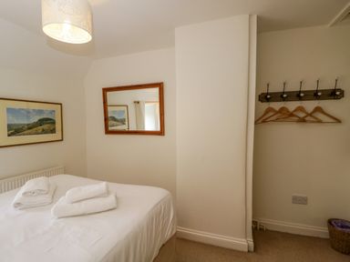 A bedroom with a bed and towels on it a mirror on the wall a painting and empty hangers on hooks at Little Owl Barn in Burford