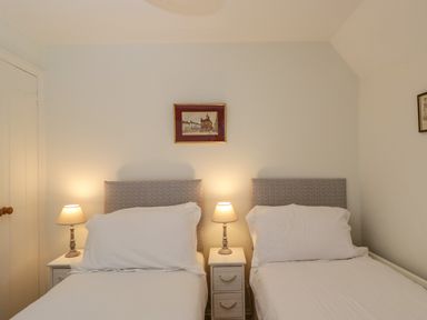 A bedroom with two single beds white bedding two bedside tables with lamps and framed pictures on walls at Little Owl Barn in Burford
