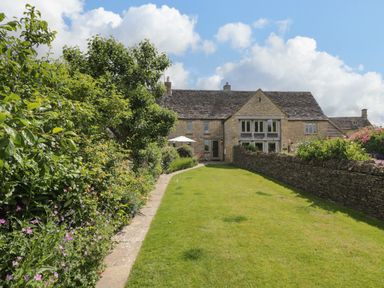A garden with a stone path lawn trees and bushes in front of a stone house at Little Owl Barn Burford