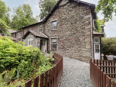 A stone house with a gravel pathway and wooden fence surrounded by greenery at Eller Close House in Grasmere