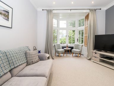 A living room with a gray sofa two armchairs and a TV by a bay window at Eller Close House in Grasmere
