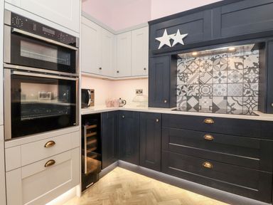 A kitchen corner with built in oven microwave wine cooler black and white cabinets and tiled backsplash at Eller Close House in Grasmere