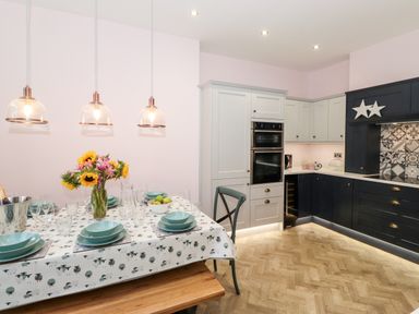 A kitchen with a dining table set with plates and glasses sunflowers on the table and pendant lights at Eller Close House in Grasmere