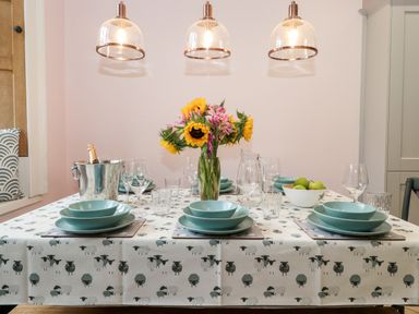A dining table set with blue dishes glassware a vase with sunflowers and pink flowers an ice bucket with a bottle and a bowl of apples at Eller Close House in Grasmere