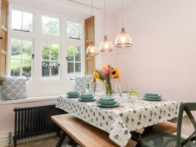 A dining table set with plates glasses and flowers near a window with cushions at Eller Close House in Grasmere