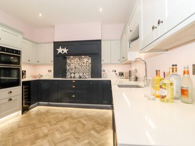 A kitchen with dark lower cabinets white upper cabinets patterned backsplash and bottles on counter at Eller Close House in Grasmere