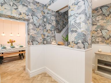 A hallway with floral wallpaper and a small table next to white wainscoting near a dining room with a set table at Eller Close House in Grasmere
