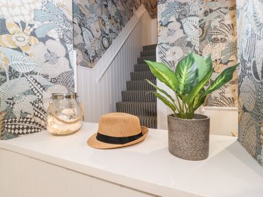 A stairway with striped carpet and floral wallpaper a plant in a pot a straw hat and a glass jar on a white ledge at Eller Close House in Grasmere