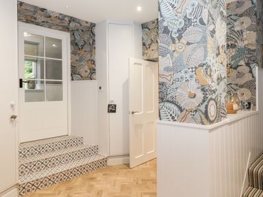 A hallway with patterned wallpaper tiled steps and a white door at Eller Close House in Grasmere