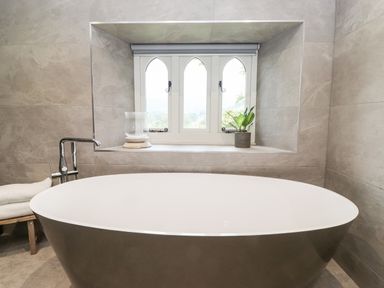 A bathroom with a freestanding bathtub under a window with three arched panes at Eller Close House in Grasmere