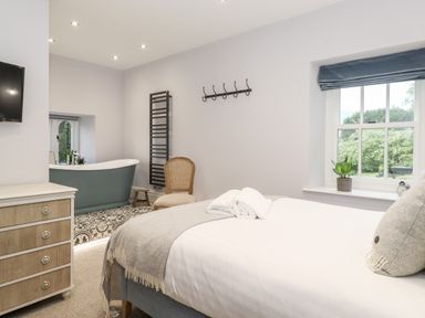A bedroom with a bed, chair, chest of drawers and a bathtub near a window at Eller Close House in Grasmere