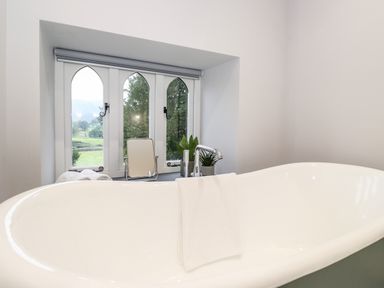 A bathroom with a bathtub in front of a window with arched panes and plants on the windowsill at Eller Close House in Grasmere