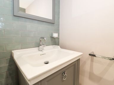 A bathroom sink with a silver faucet a mirror above and green tiled wall at Eller Close House in Grasmere