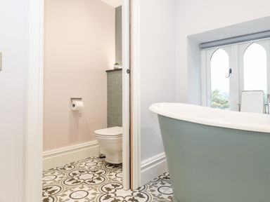 A bathroom with a green freestanding bathtub and a separate toilet area with patterned floor tiles at Eller Close House in Grasmere