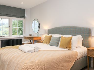A bedroom with a bed with three pillows two bedside tables a wooden desk with a mirror and window at Eller Close House in Grasmere