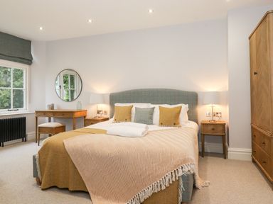 A bedroom with a double bed with pillows and blankets a wooden desk with a chair a round mirror bedside tables with lamps and a wooden wardrobe at Eller Close House in Grasmere