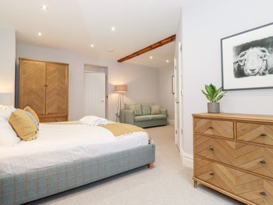A bedroom with a bed sofa wooden wardrobe wooden dresser a framed picture and a lamp at Eller Close House in Grasmere