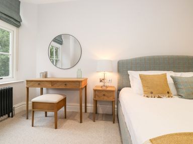 A bedroom with a bed with pillows a bedside table with a lamp a dressing table with a stool and a round mirror at Eller Close House in Grasmere