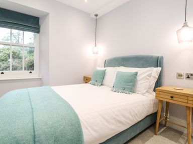 A bedroom with a bed with teal pillows and blanket two wooden bedside tables and hanging lights at Eller Close House in Grasmere