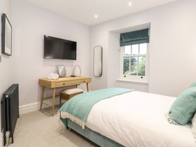 A bedroom with a bed and a wooden desk under a wall mounted TV at Eller Close House in Grasmere