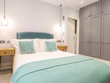 A bedroom with a bed and teal cushions and throw next to wooden bedside tables and a wall of gray wardrobes at Eller Close House in Grasmere