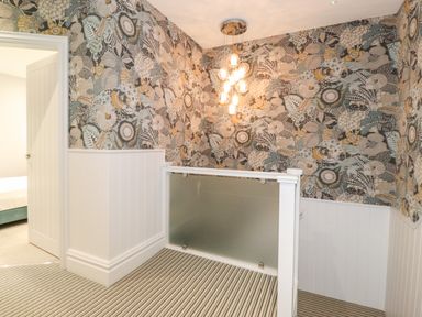 A stairway landing with floral wallpaper white wooden paneling striped carpet and a hanging light fixture at Eller Close House in Grasmere
