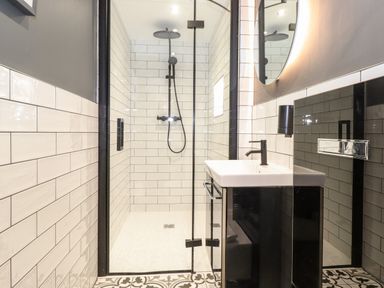 A bathroom with a walk-in shower a black faucet a round mirror and patterned floor tiles at Eller Close House in Grasmere
