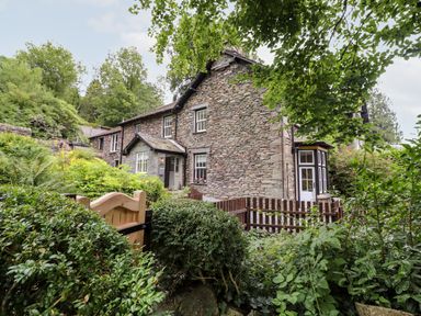 A stone house with white windows and wooden fence surrounded by greenery at Eller Close House in Grasmere