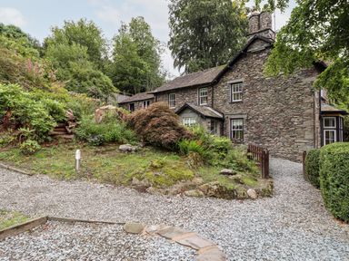 A stone house with multiple windows surrounded by greenery and gravel paths at Eller Close House in Grasmere