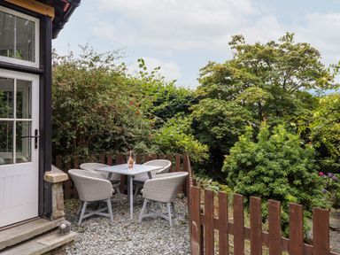 A small outdoor patio area with a table and four chairs surrounded by plants and a wooden fence at Eller Close House in Grasmere