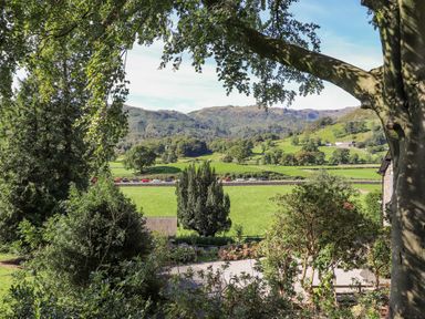 A rural landscape with trees a grassy field and hills in the background at Eller Close House in Grasmere