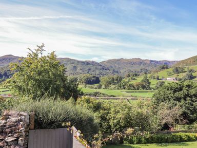 A rural landscape with trees bushes and hills under a blue sky at Eller Close House in Grasmere
