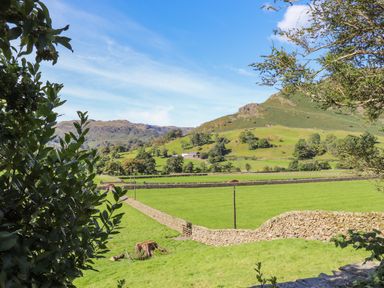 A rural landscape with green fields stone walls trees and hills in the background at Eller Close House in Grasmere