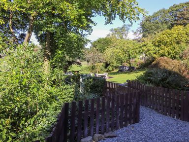 A garden with trees shrubs a wooden fence and an outdoor seating area at Eller Close House in Grasmere