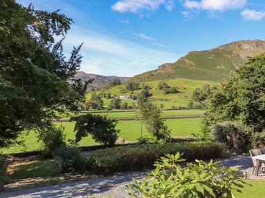 A garden with bushes and trees overlooking green fields and hills at Eller Close House in Grasmere