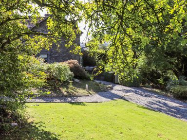 A garden with a gravel path and green grass surrounded by trees and bushes at Eller Close House in Grasmere