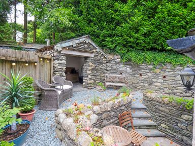 A garden with stone walls and furniture at Fellside Cottage in Bowness-On-Windermere