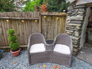 A garden with a wicker bench and a topiary planter at Fellside Cottage in Bowness-On-Windermere